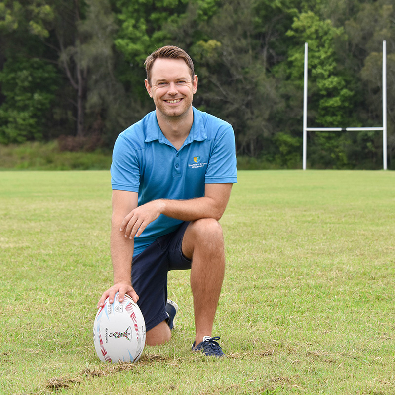 Christian Swann kneeling with football on sports field