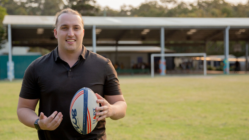 Man holding a rugby ball while standing on a sports ground
