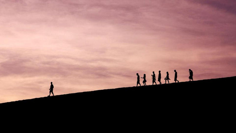 Silhouette of people walking down a hill at sunrise