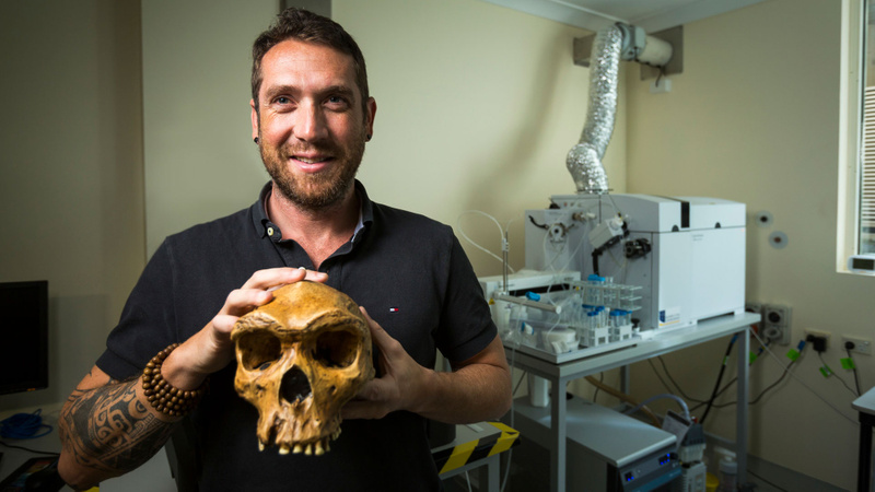 Dr Renaud Joannes-Boyau holding a human scull with lab equipment in background