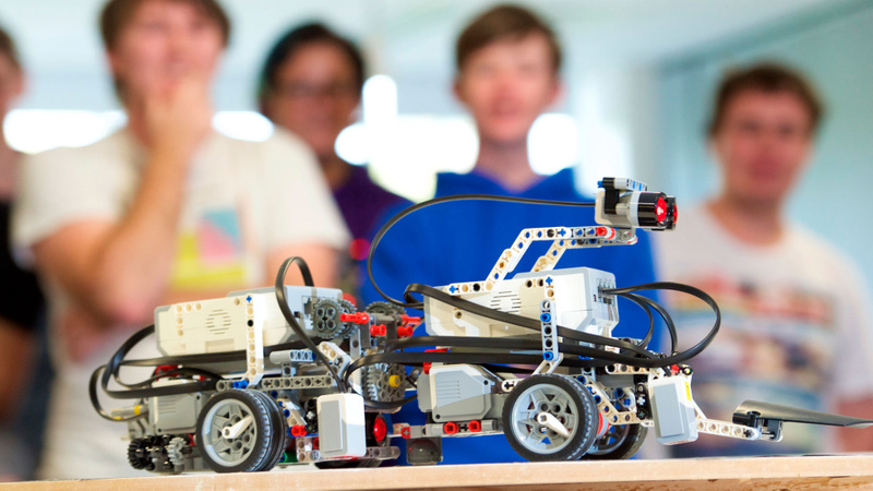 Blurred students in background looking at a lego cart robot