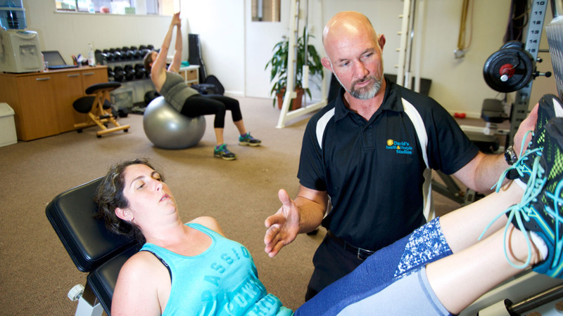 Personal trainer helps woman working on leg press machine
