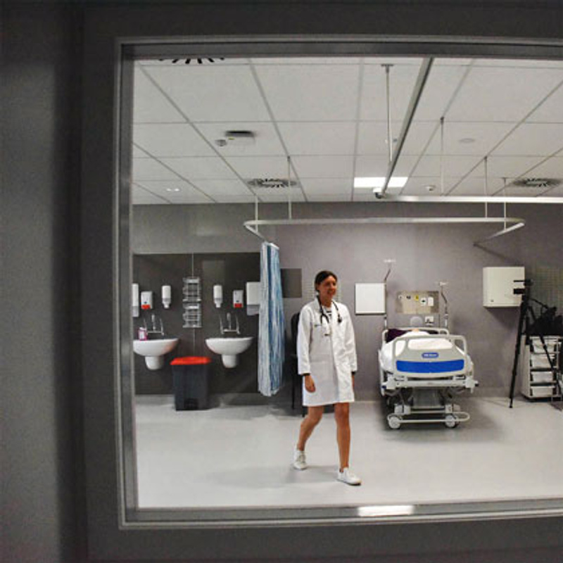 Woman in white coat walks past hospital bed