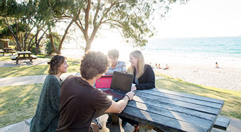 Group of international students sitting at table with beach in background