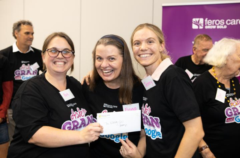 Three smiling women wearing the same t-shirt holding an envelope