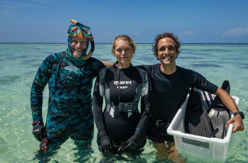 A woman and two men in wetsuits at a reef