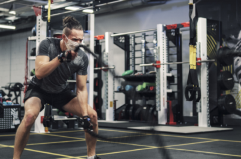 Man wearing a mask while exercising with battle ropes in the gym