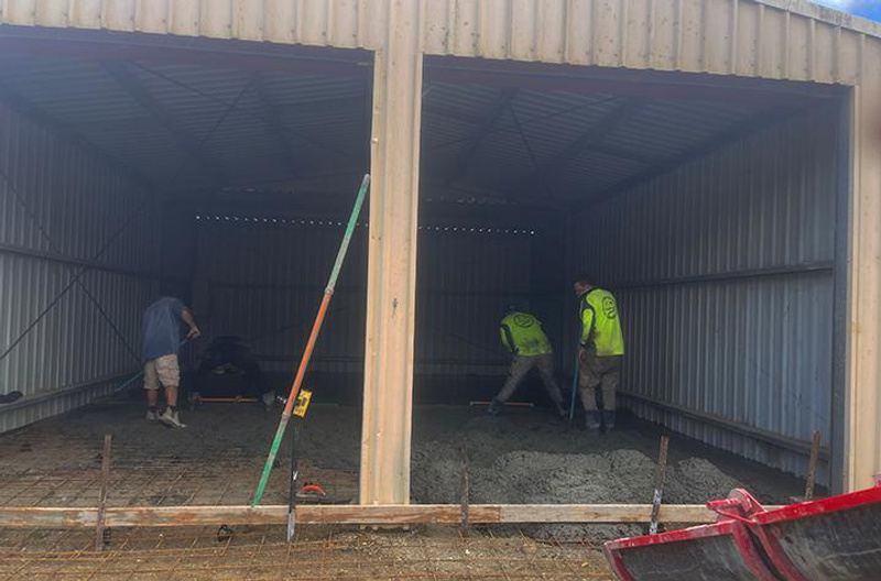 Workers level concrete floor inside shed
