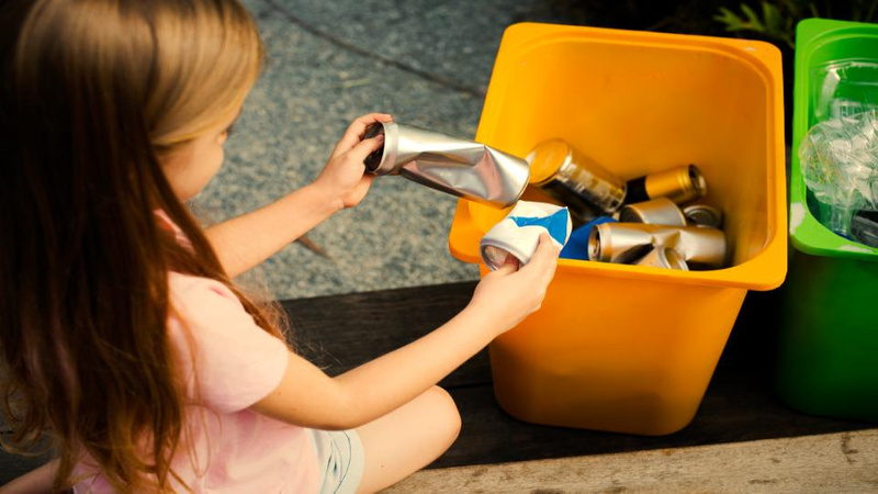 Young girl recycling cans into bin