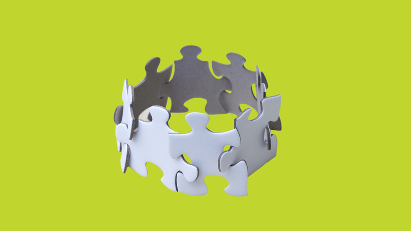 numerous white puzzle pieces interlinked to a circle to resemble people linking arms on a green background