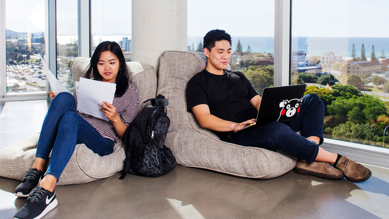 Two students studying with beach in the background