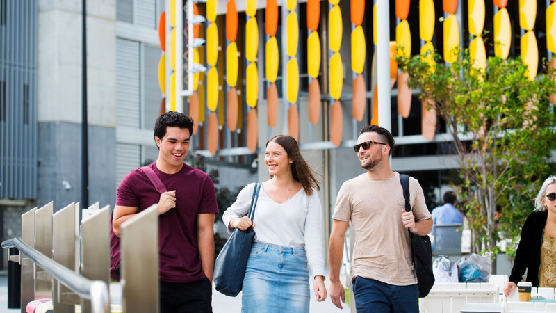 Three students walking together chatting outside a colourful building 